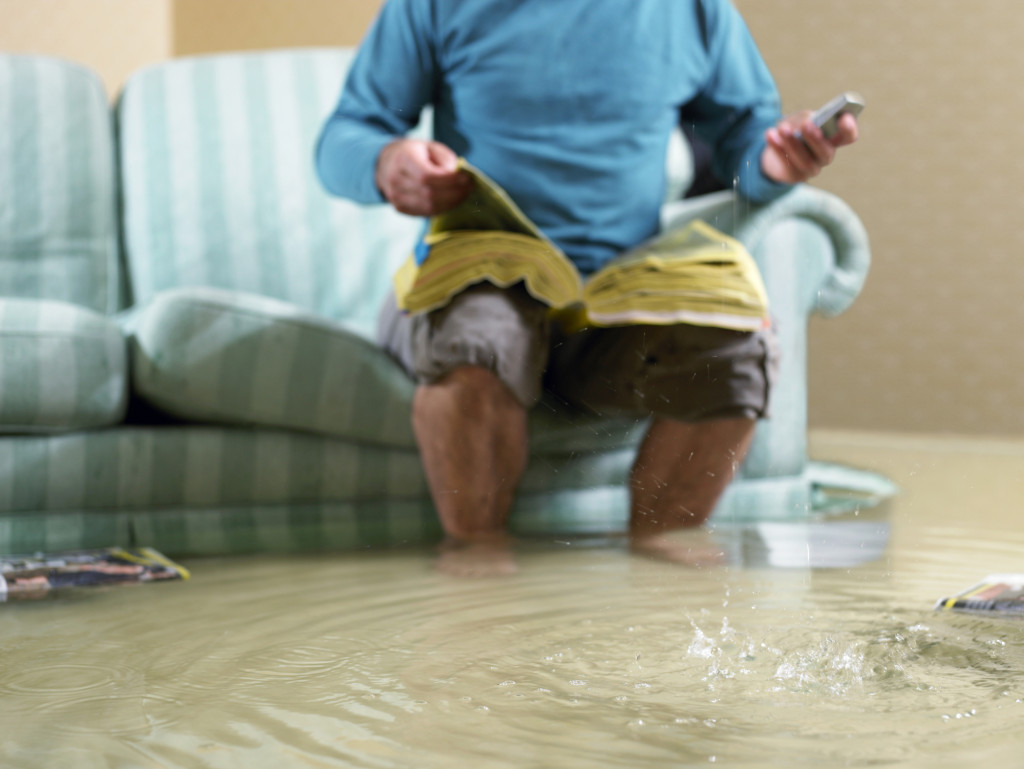 Man sitting in flooded living room using phone, low section
